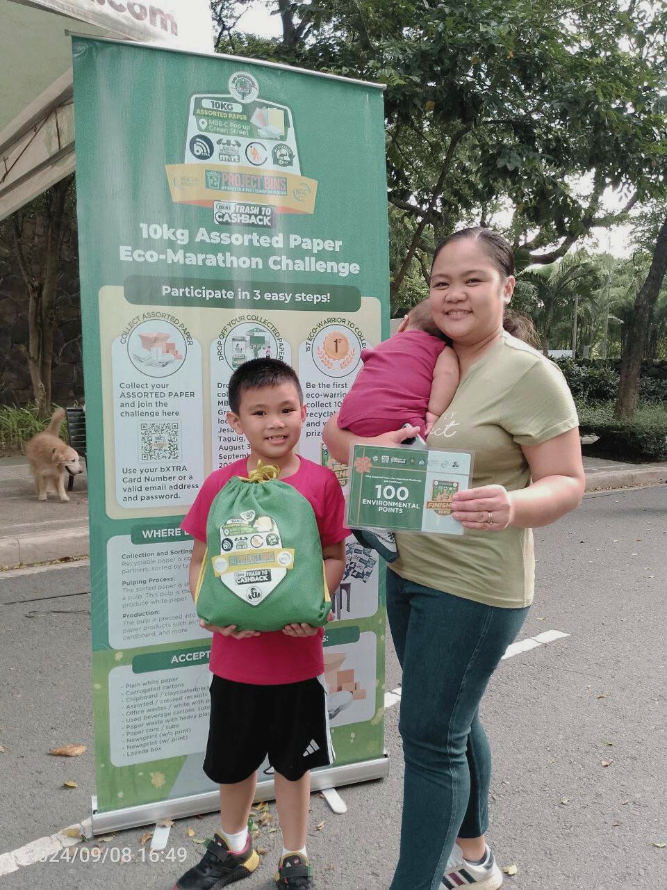 A mother and child joining the 10 kg Assorted Paper Eco-Marathon Challenge beside the program banner