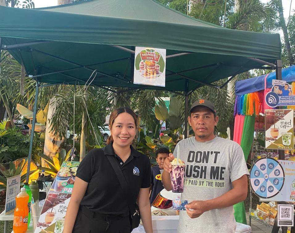 Residents at a Trash to Cashback booth beside a partner store redemption poster