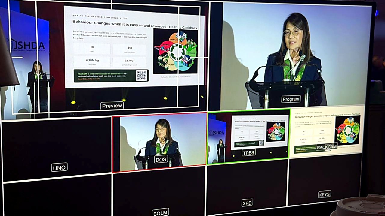 Broadcast monitors showing the Trash to Cashback five pillars slide during the address